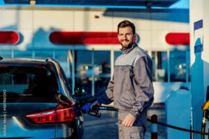 A gas station worker filling up car tank and smiling at the camera.